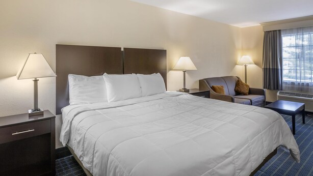 A hotel room with a large bed, two bedside tables with lamps, a chair, and a window with curtains.