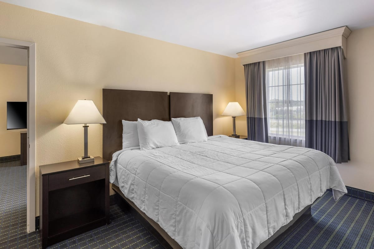 A hotel room with a large bed, two bedside tables with lamps, a flat-screen TV, and a window with curtains.