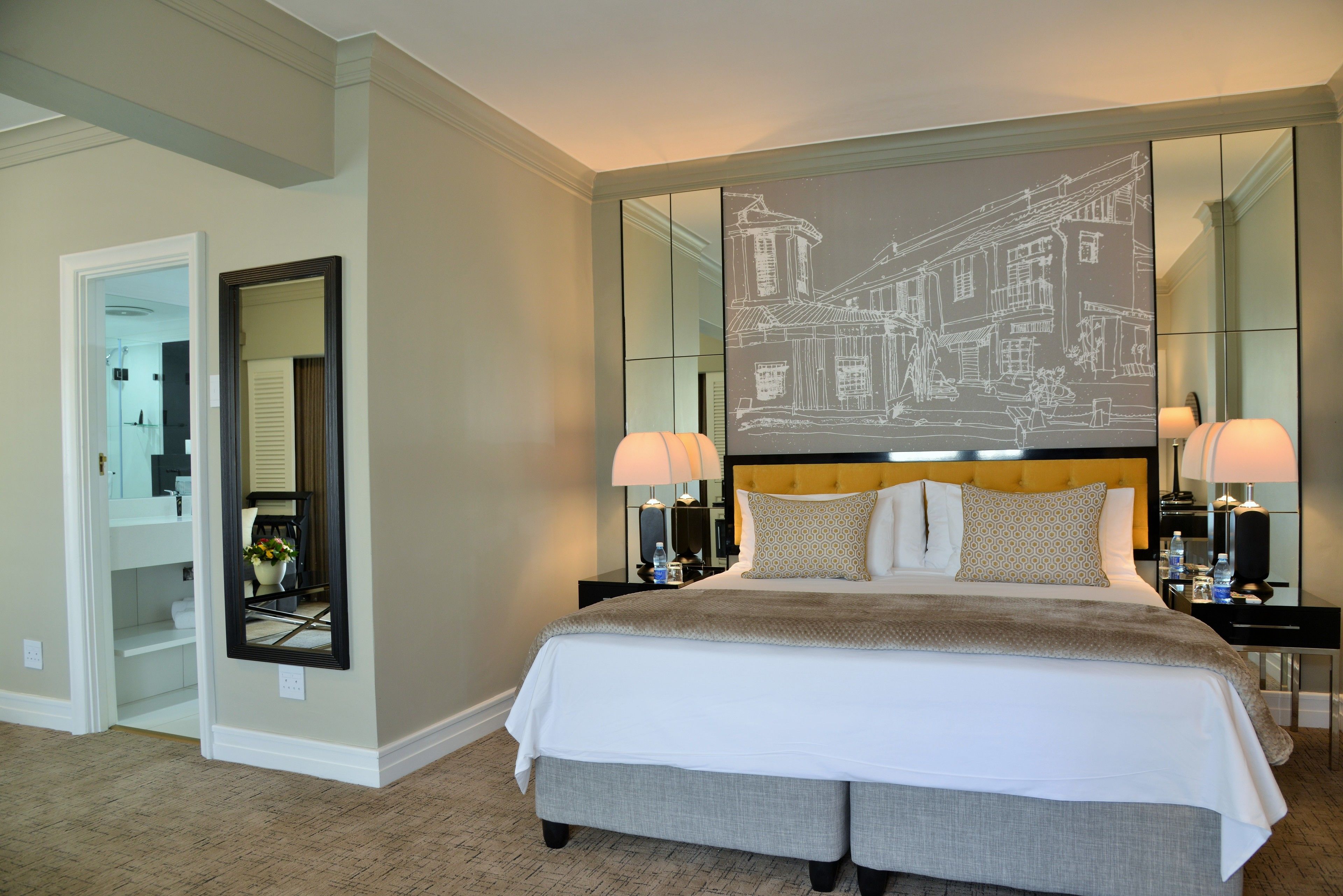 A neatly arranged bedroom with a large bed, a headboard with a cityscape mural, two bedside tables with lamps, and a full-length mirror.