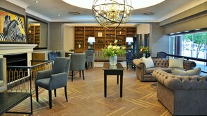A spacious living area with a fireplace, modern furniture, a large chandelier, and a view of the outdoors. - Capetonian Hotel (Cape Town)