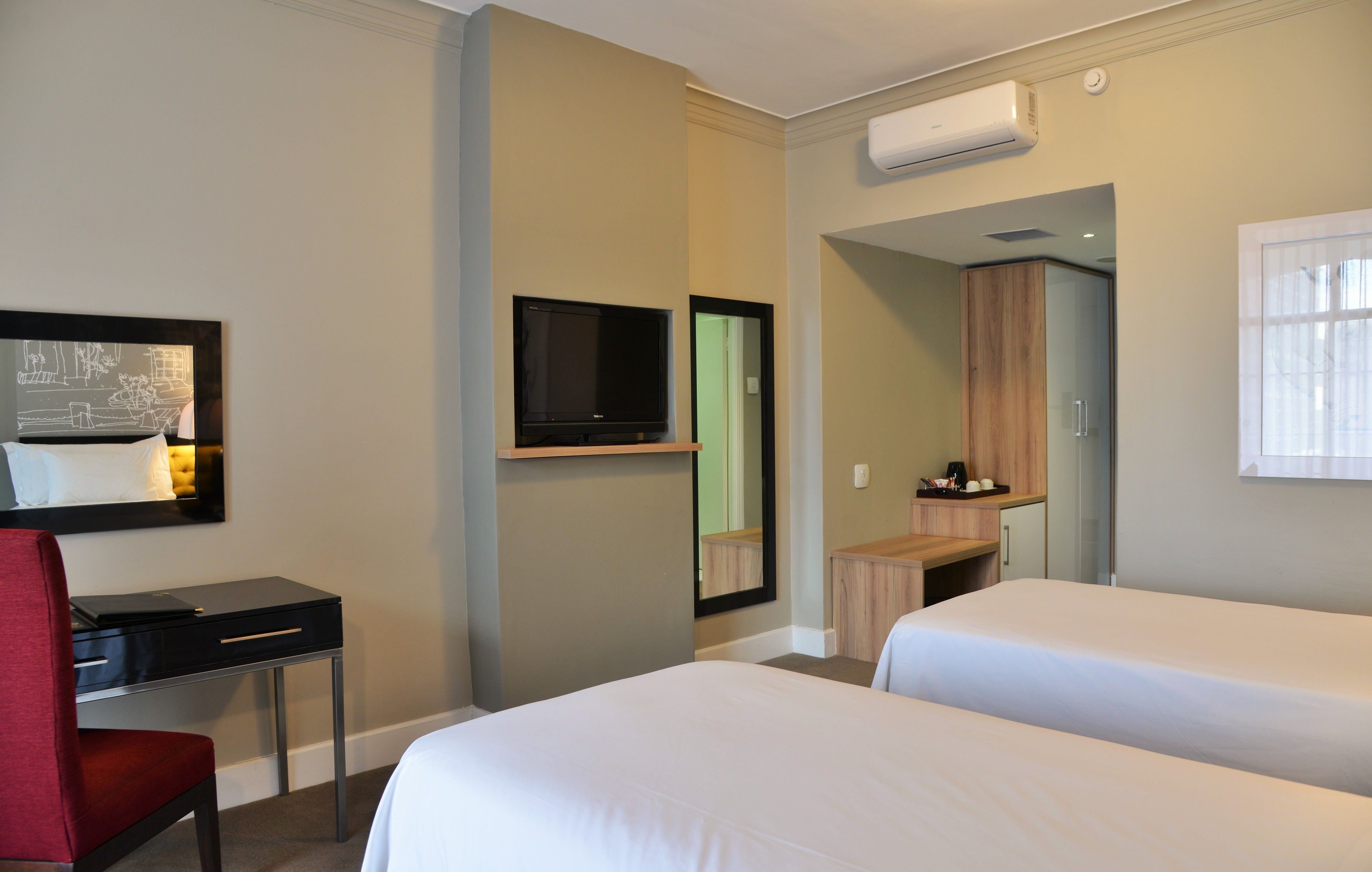 A hotel room with two beds, a desk, a chair, a TV, and a wardrobe.