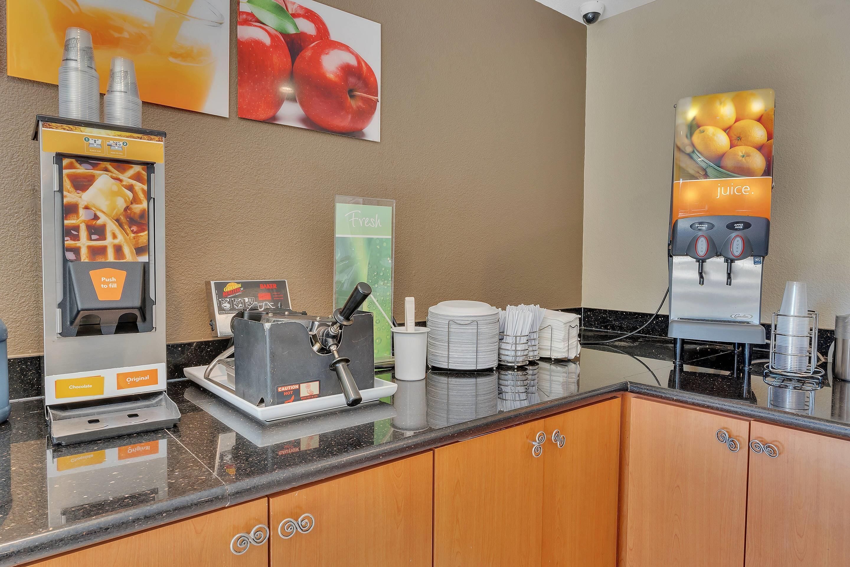 Un buffet de petit-déjeuner en libre-service proposant des gaufres, du chocolat et d'autres options originales, ainsi qu'une machine à café et un distributeur de jus de fruits.