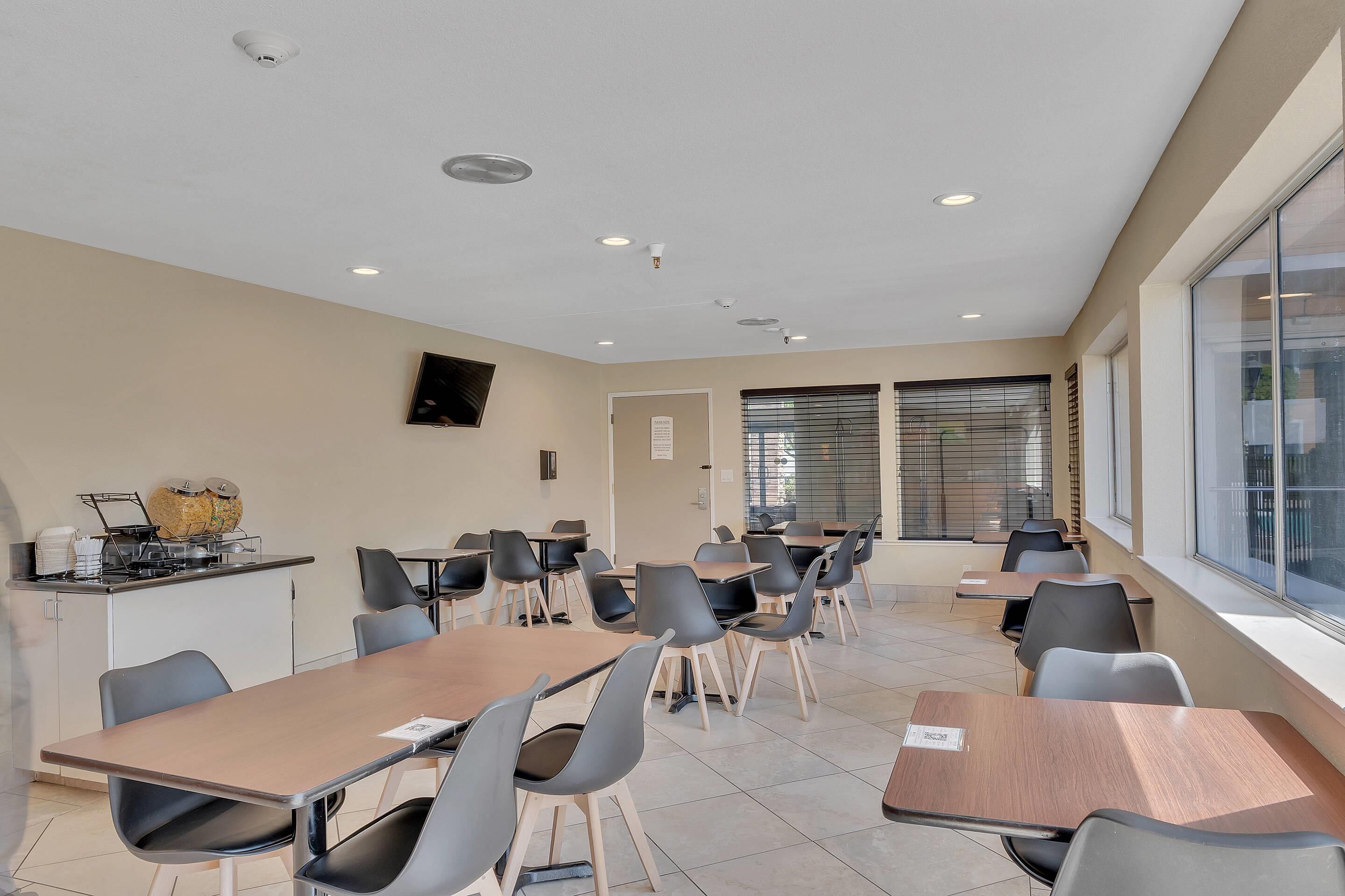 A conference room with tables and chairs, a kitchenette, and large windows.