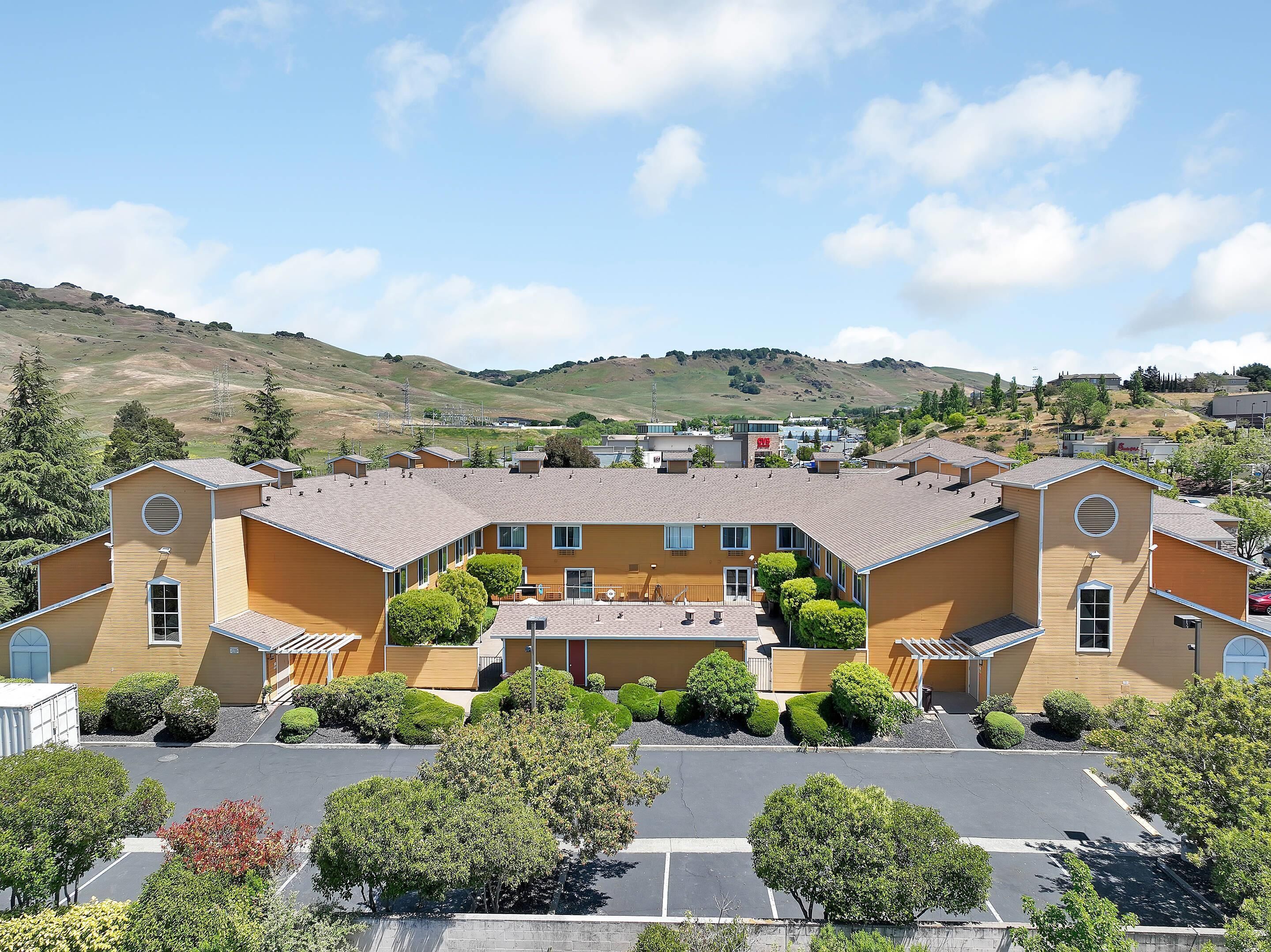 A large, yellow building with multiple wings and a central courtyard, surrounded by parking and greenery.
