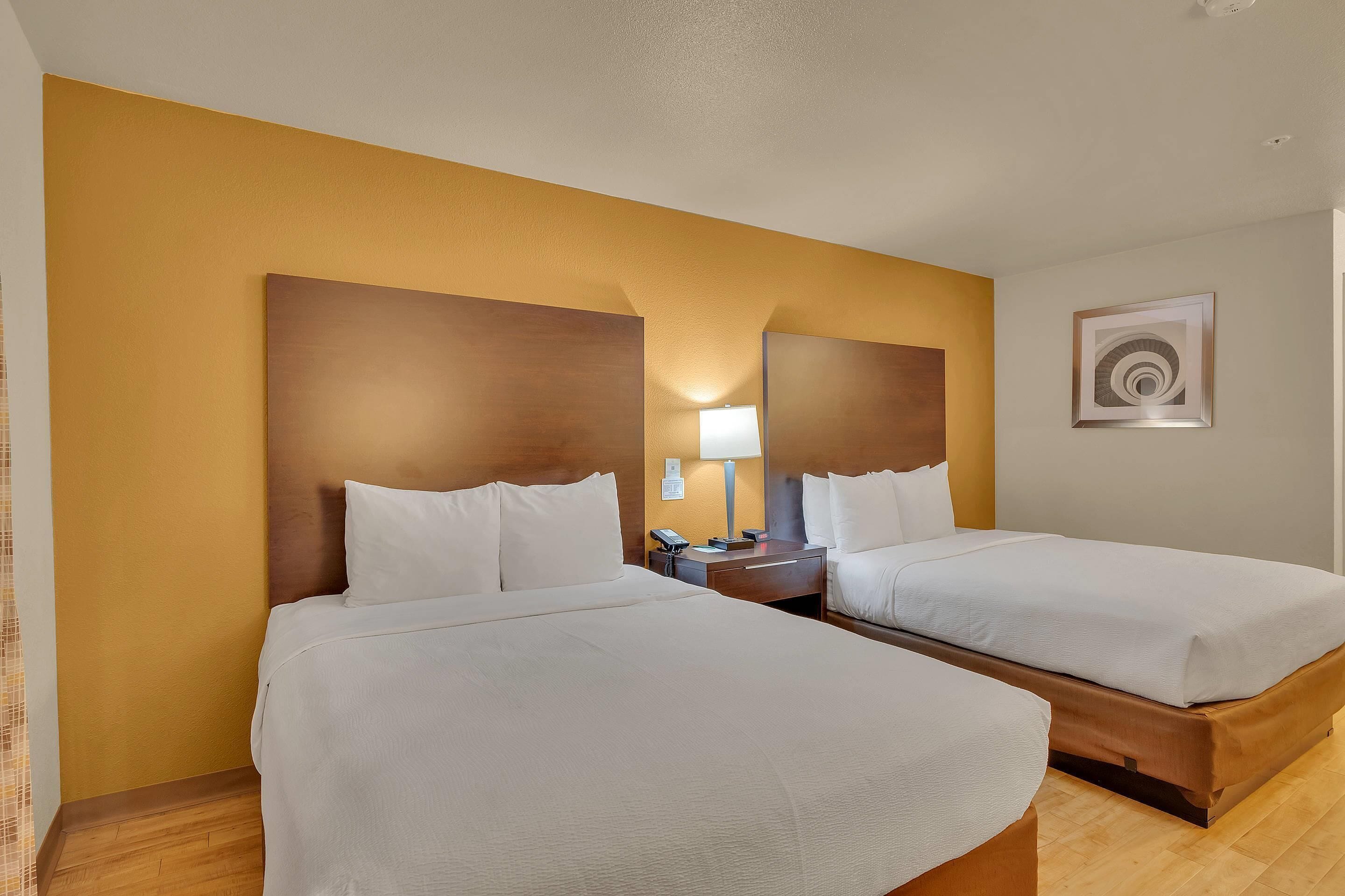 A hotel room with two beds, a nightstand with a lamp, and a framed artwork on the wall.