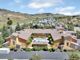 Um edifício grande com piscina, rodeado por arbustos e árvores bem cuidados.
