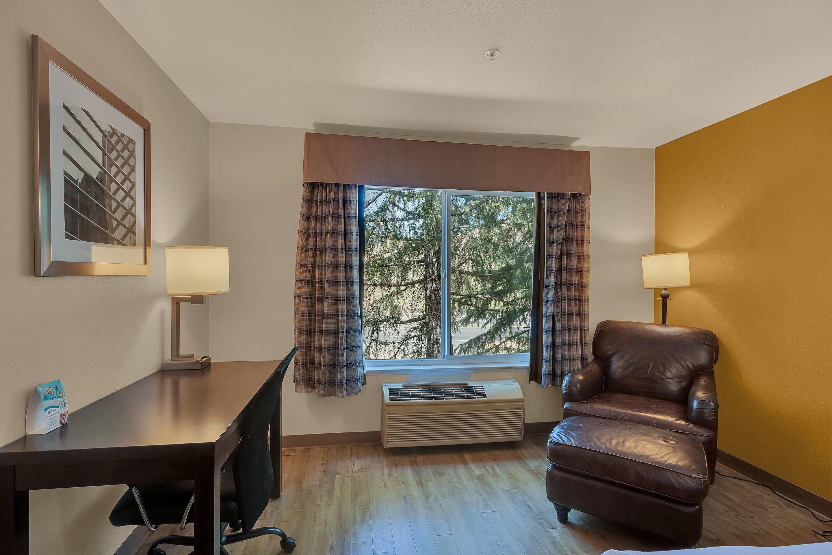 Habitación de hotel con escritorio, silla, dos lámparas, ventana con cortinas y un radiador.
