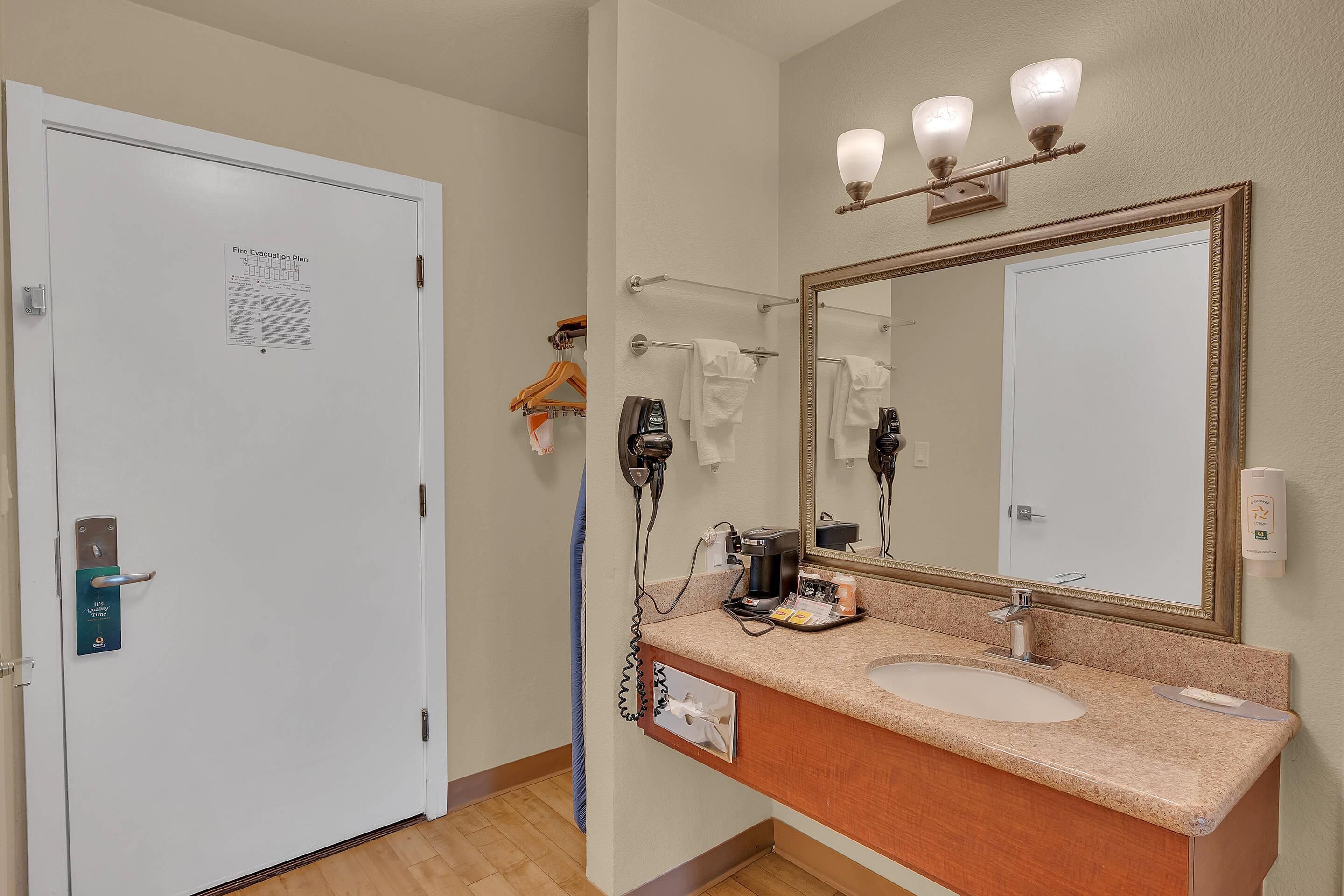 A hotel bathroom with a white door, a large mirror, a sink, and a towel rack.