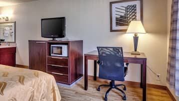 Une chambre d’hôtel comprenant un lit, un bureau avec une chaise, une télévision, une lampe et un tableau encadré au mur.