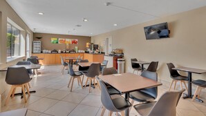 A modern dining area with tables and chairs, a kitchen counter, and a mounted TV.