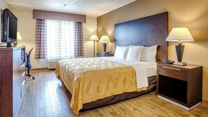 A hotel room with a large bed, two bedside tables with lamps, a TV on a dresser, and a window with curtains.