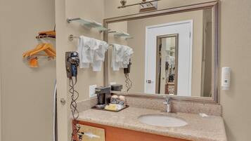 A hotel bathroom with a granite countertop, a sink, a mirror, towel racks, and a coffee machine.