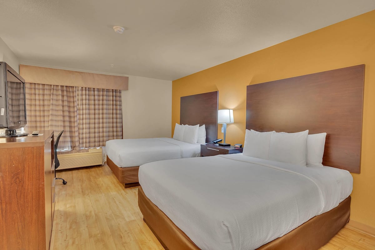 A hotel room with two beds, a desk, a chair, a TV, and a window with curtains.