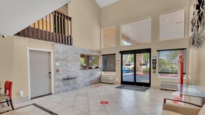 A spacious lobby with a high ceiling, a staircase, a reception desk, and a glass partition.