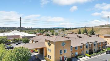 A multi-story hotel with a flat roof, a parking lot, and a view of a hilly landscape in the background.
