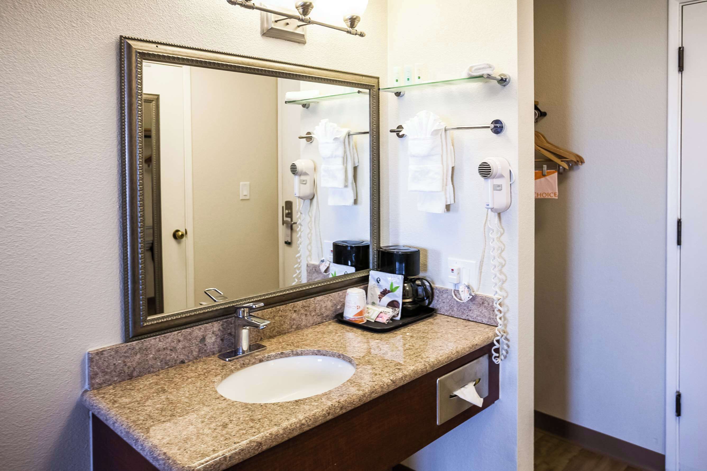 A bathroom with a sink, mirror, towel rack, hairdryer, and a coffee maker.