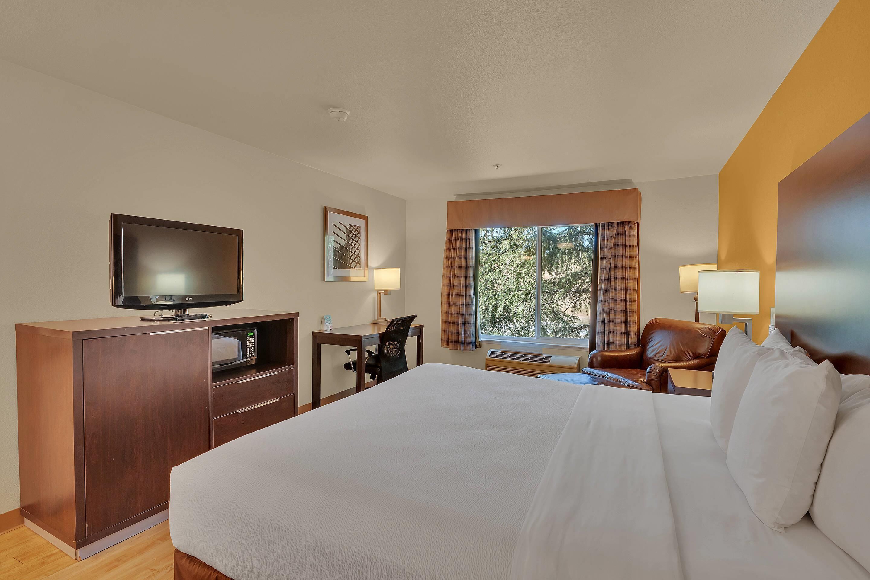 A hotel room with a large bed, a desk with a computer, a television, and a window with curtains.