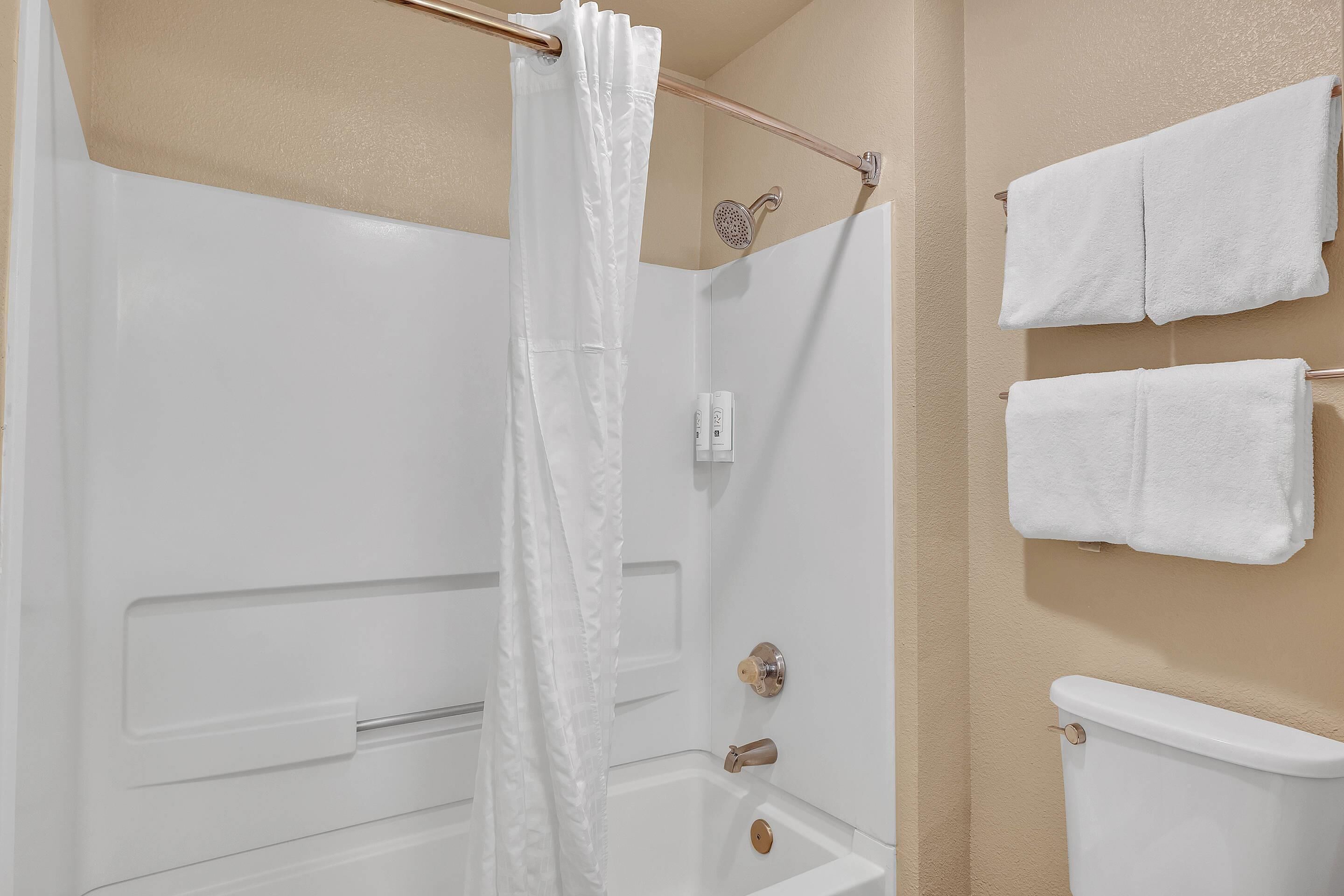 Ein Badezimmer mit Badewanne, Dusche und Toilette. Zwei weiße Handtücher hängen an der Wand.