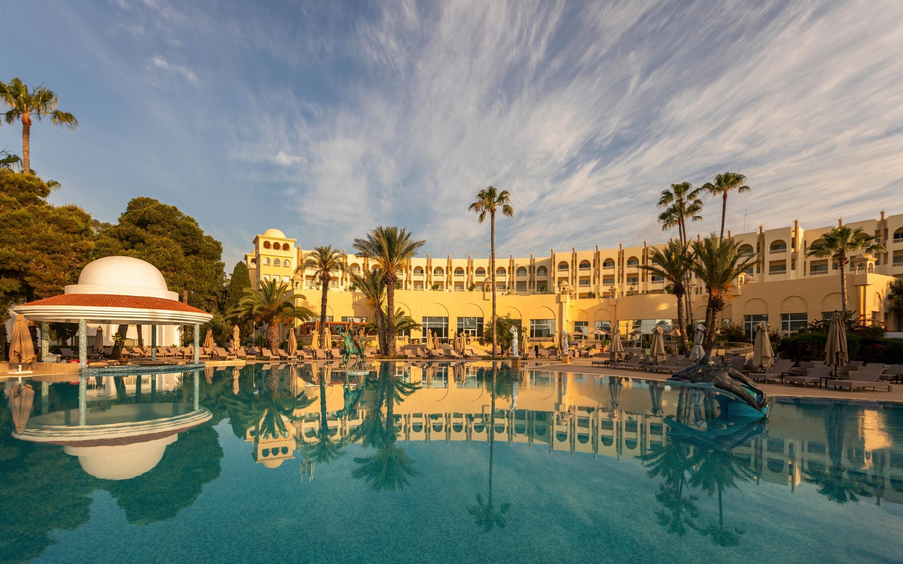 A resort with a large pool, palm trees, and a building with multiple balconies.