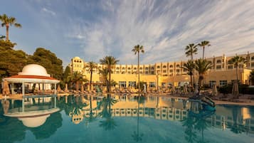 Un resort con una piscina grande, palmeras y un edificio con varios balcones.