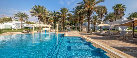 A swimming pool with clear blue water, surrounded by palm trees and lounge chairs.