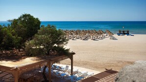 Ein Strand mit Reihen von Liegestühlen und Sonnenschirmen, einer Holzpergola und freiem Blick auf das Meer.