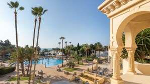 Een resort met een zwembad, palmbomen, buitenzitplaatsen en een klassieke boog.
