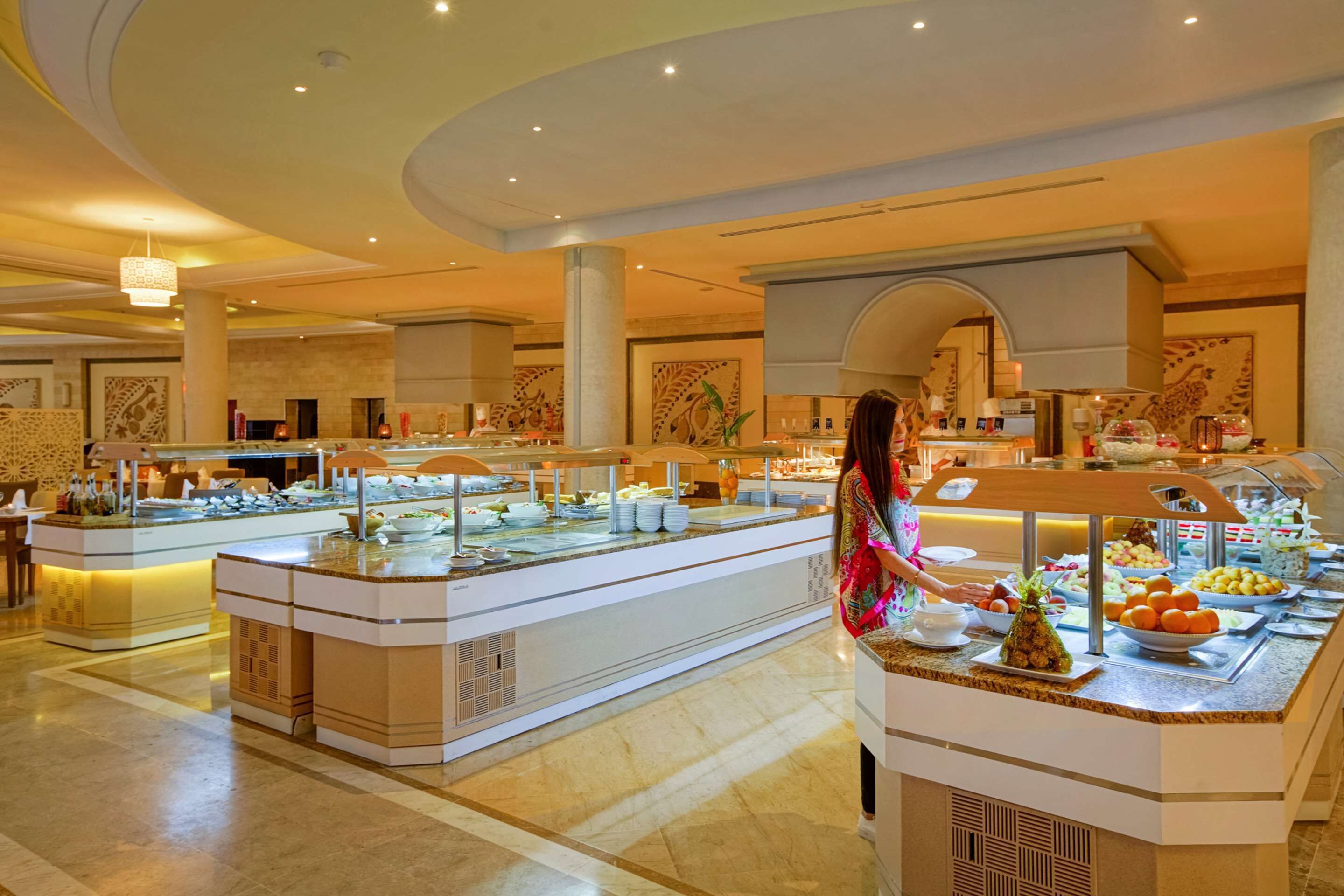 Zona de buffet con varias estaciones de servicio, una mujer sirviendo comida y una variedad de platos a la vista.