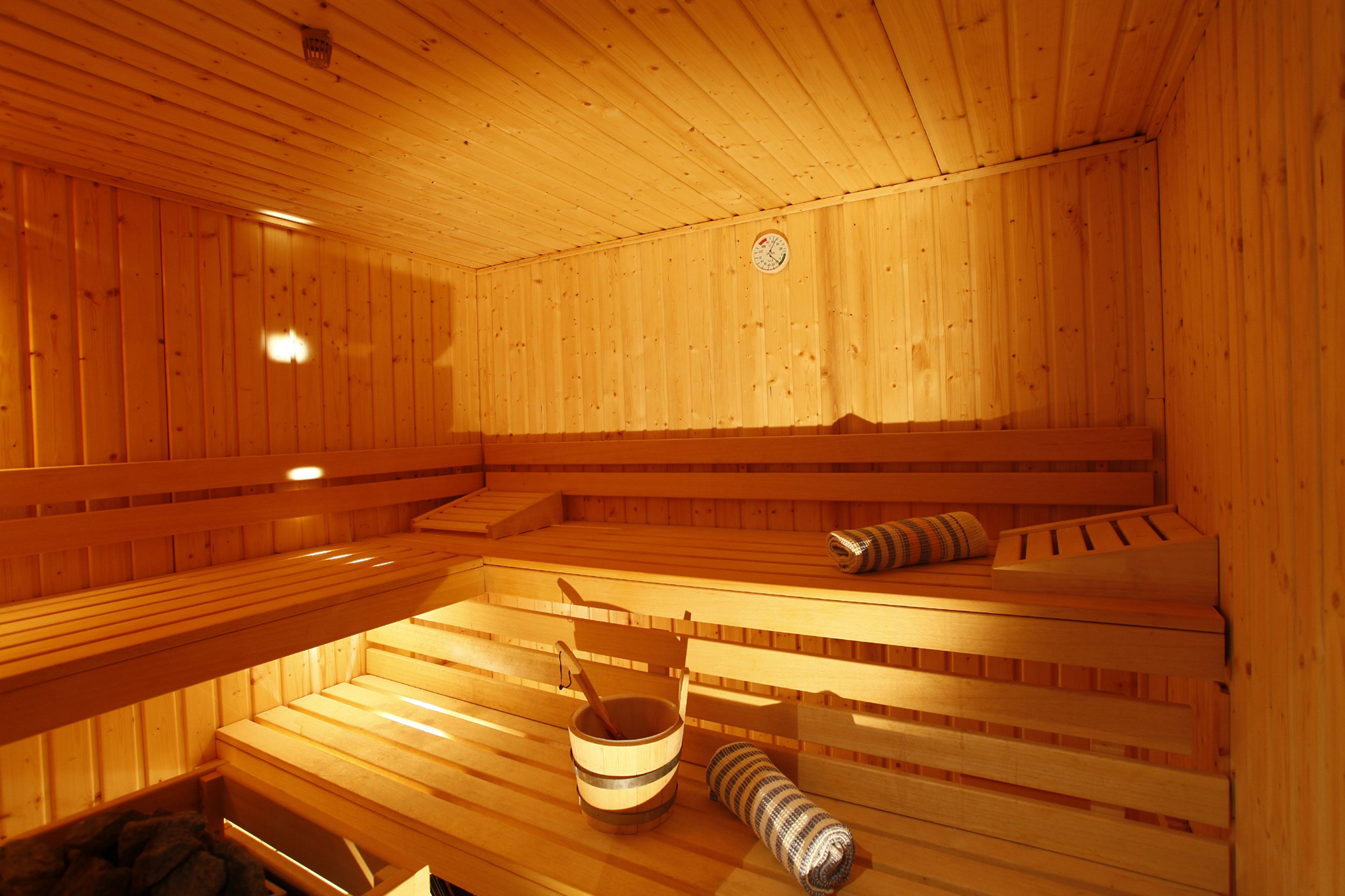 Una sauna con bancos de madera, un balde de madera y una toalla enrollada.
