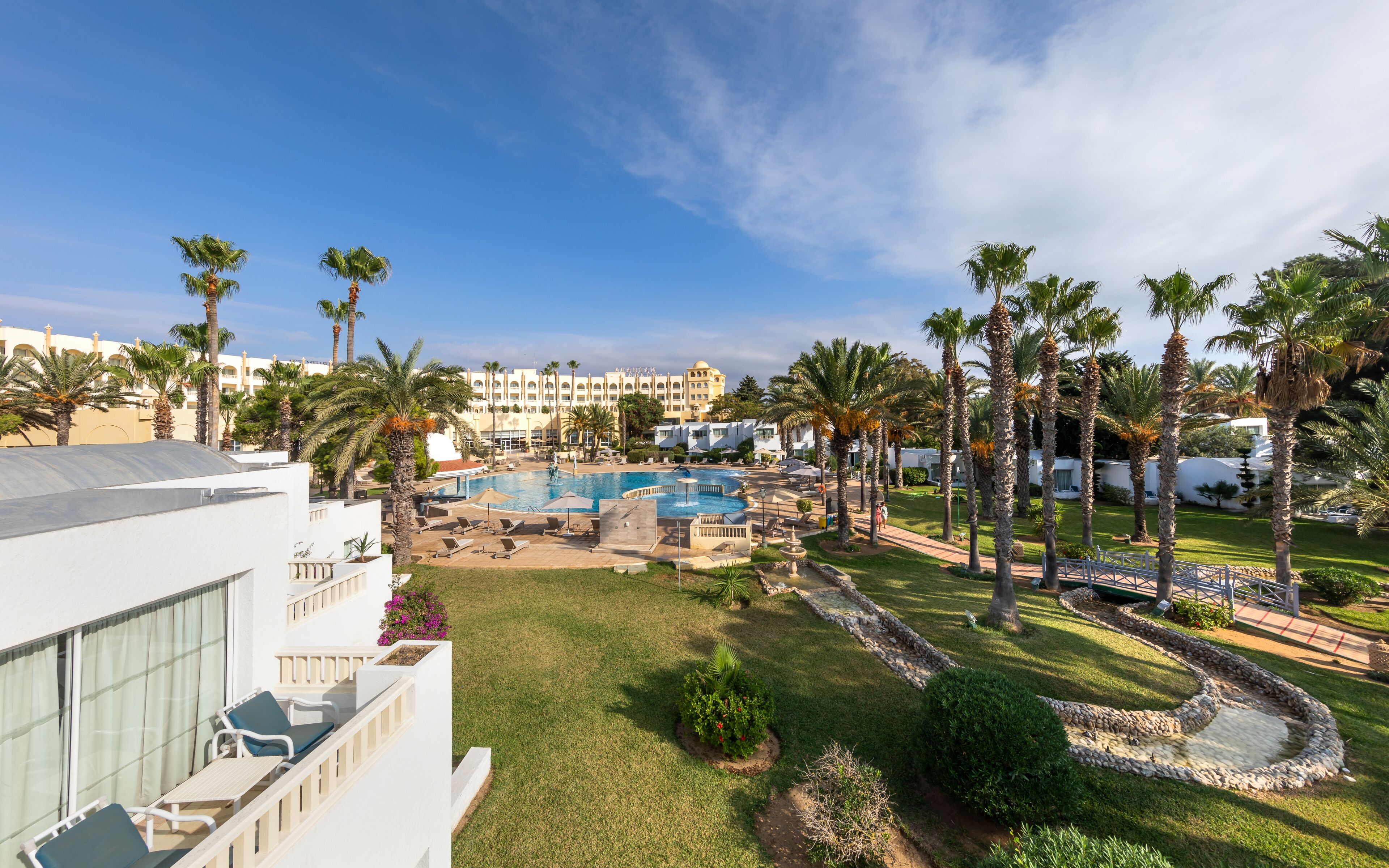 Een resort met een zwembad, palmbomen en een gebouw met een witte gevel.