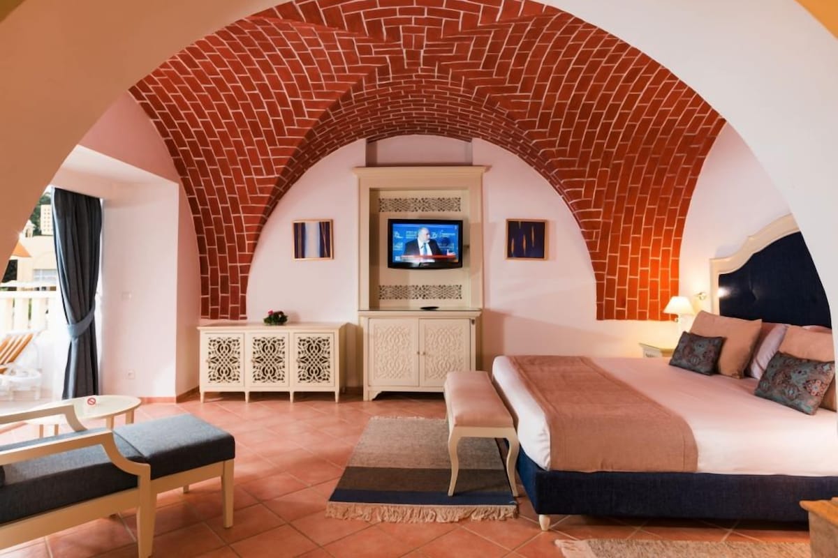 Ein Schlafzimmer mit Ziegelbogen, Fernseher, Bett, Sitzbank und kleinem Tisch.