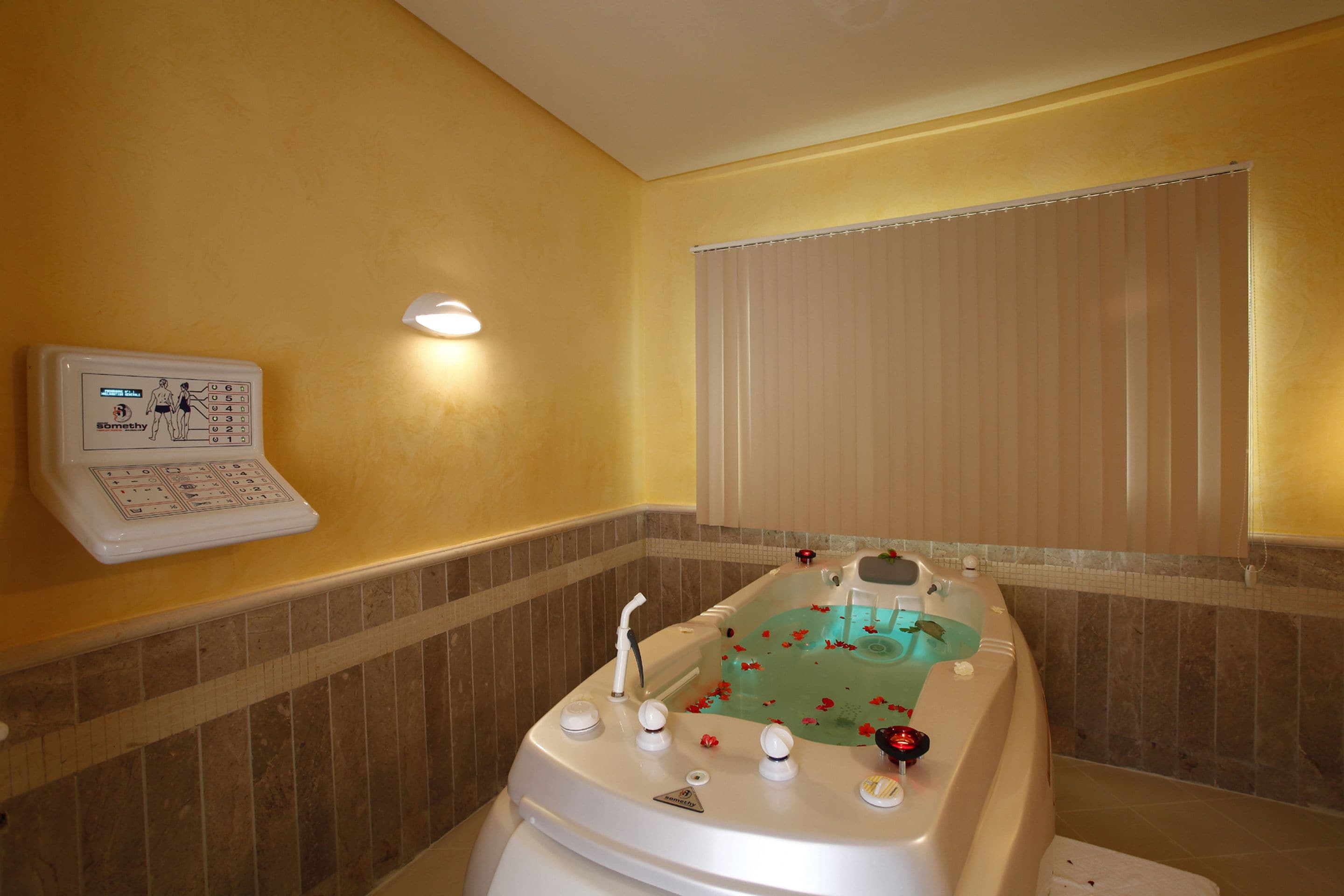 Ein Badezimmer mit einer Badewanne, einer Bedienkonsole und einem Fenster mit Jalousien.
