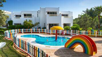 A swimming pool with a rainbow play structure and a white building in the background.