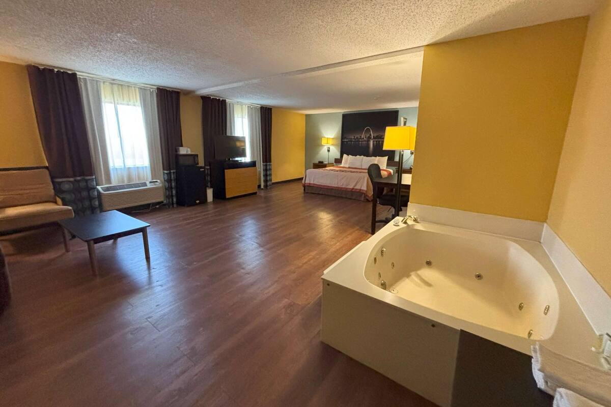 A hotel room with a large bathtub, a bed, a desk, a chair, and a sofa.