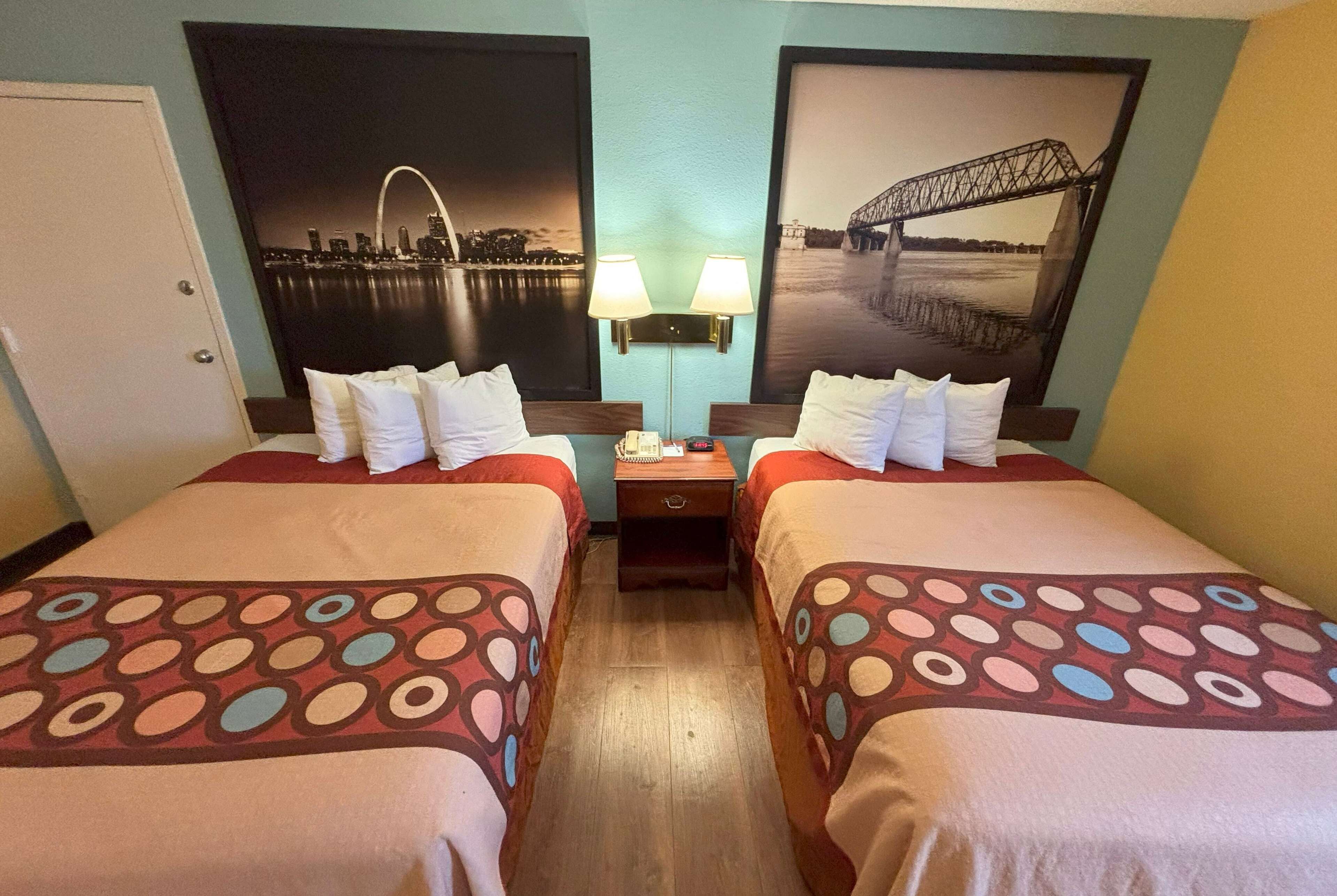 Une chambre d’hôtel avec deux lits, chacun recouvert d’une couvre-lit à motifs, une table de chevet avec une lampe et deux lampes fixées au mur.