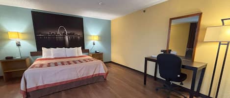 Habitación de hotel con cama, escritorio, silla, mesita de noche y un espejo instalado en la pared.