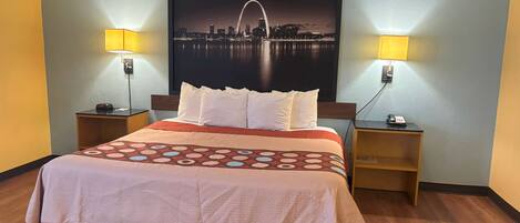 Quarto de hotel com cama, duas luminárias de cabeceira, mesa de apoio, telefone fixado na parede e pôster de paisagem urbana.