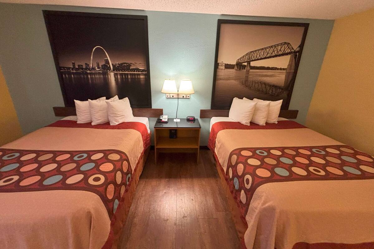 A hotel room with two beds, a nightstand, a lamp, and two wall-mounted pictures.