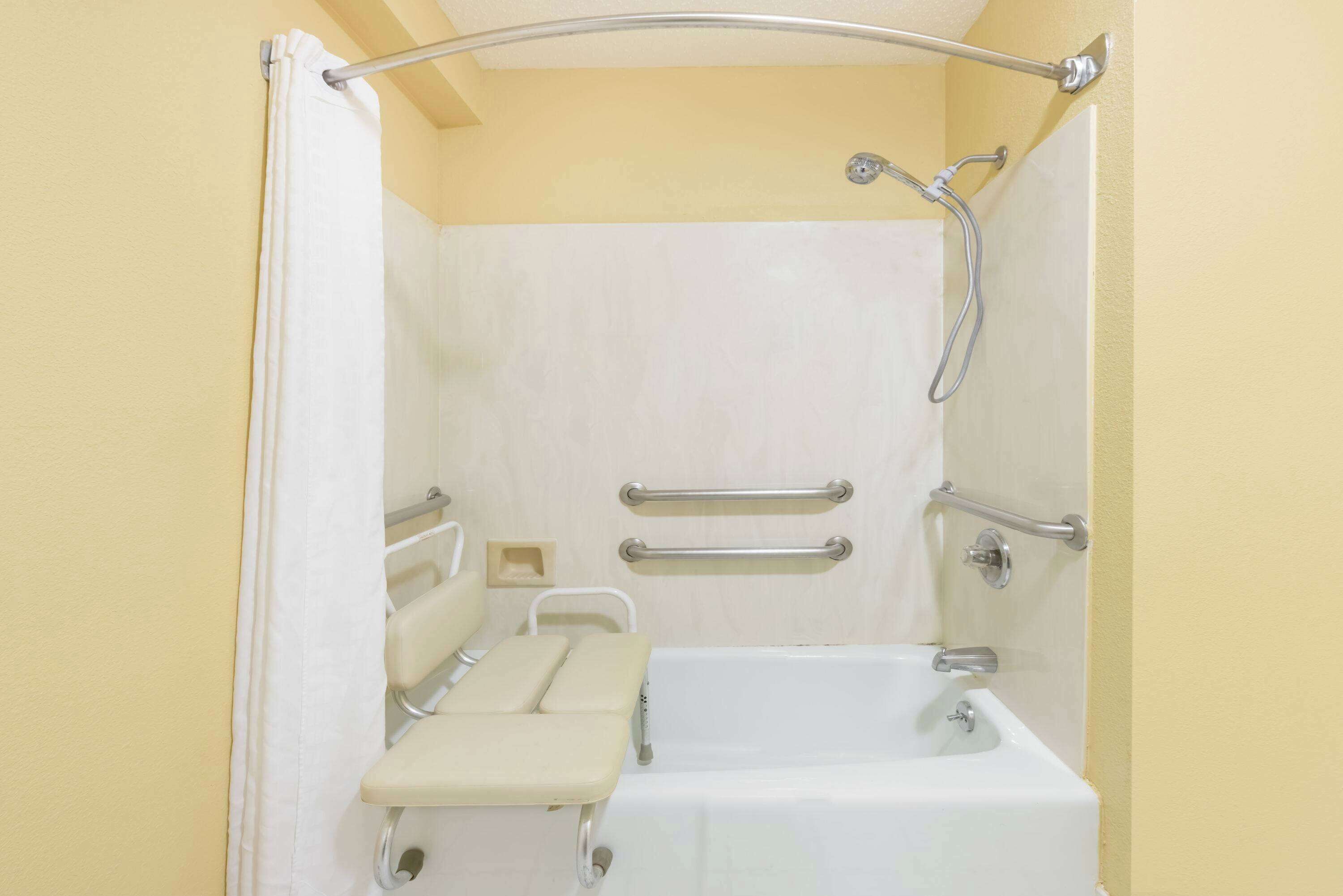 A bathroom with a bathtub, a shower, and a toilet. It includes grab bars and a bench.