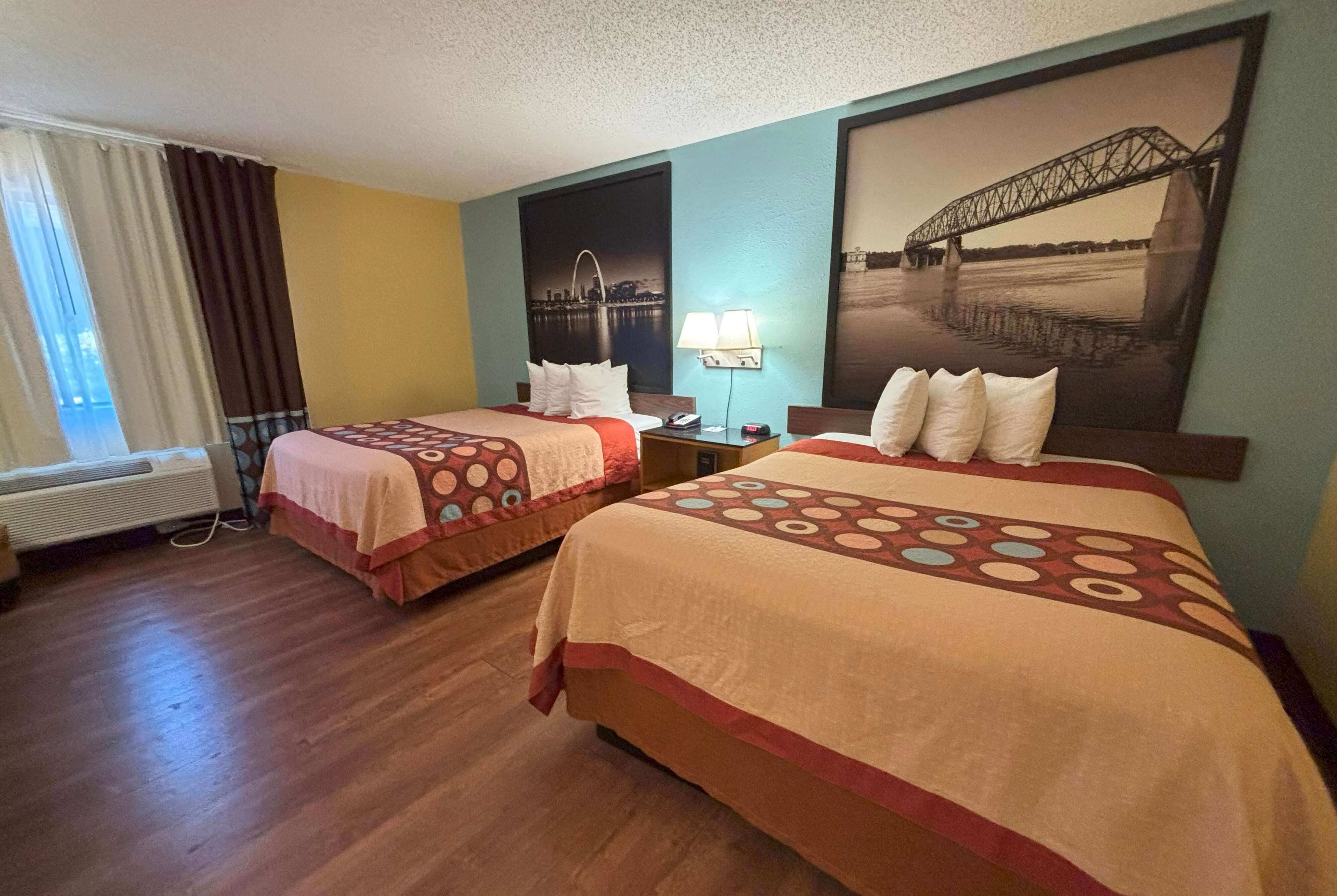 Een hotelkamer met twee bedden, een raam met gordijnen, een wandlamp en een groot, ingelijst beeld van een brug.