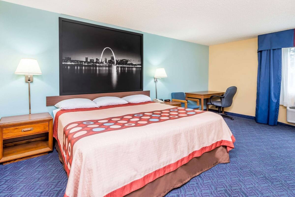 A hotel room with a bed, desk, chair, and two bedside lamps.