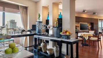 A modern kitchen with a dining area, featuring a large window, a fruit bowl, and a variety of kitchenware.