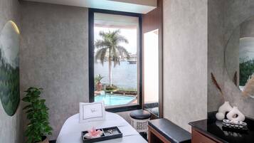 A spa room with a bed, a small table with a tray, a potted plant, and a view of a body of water.