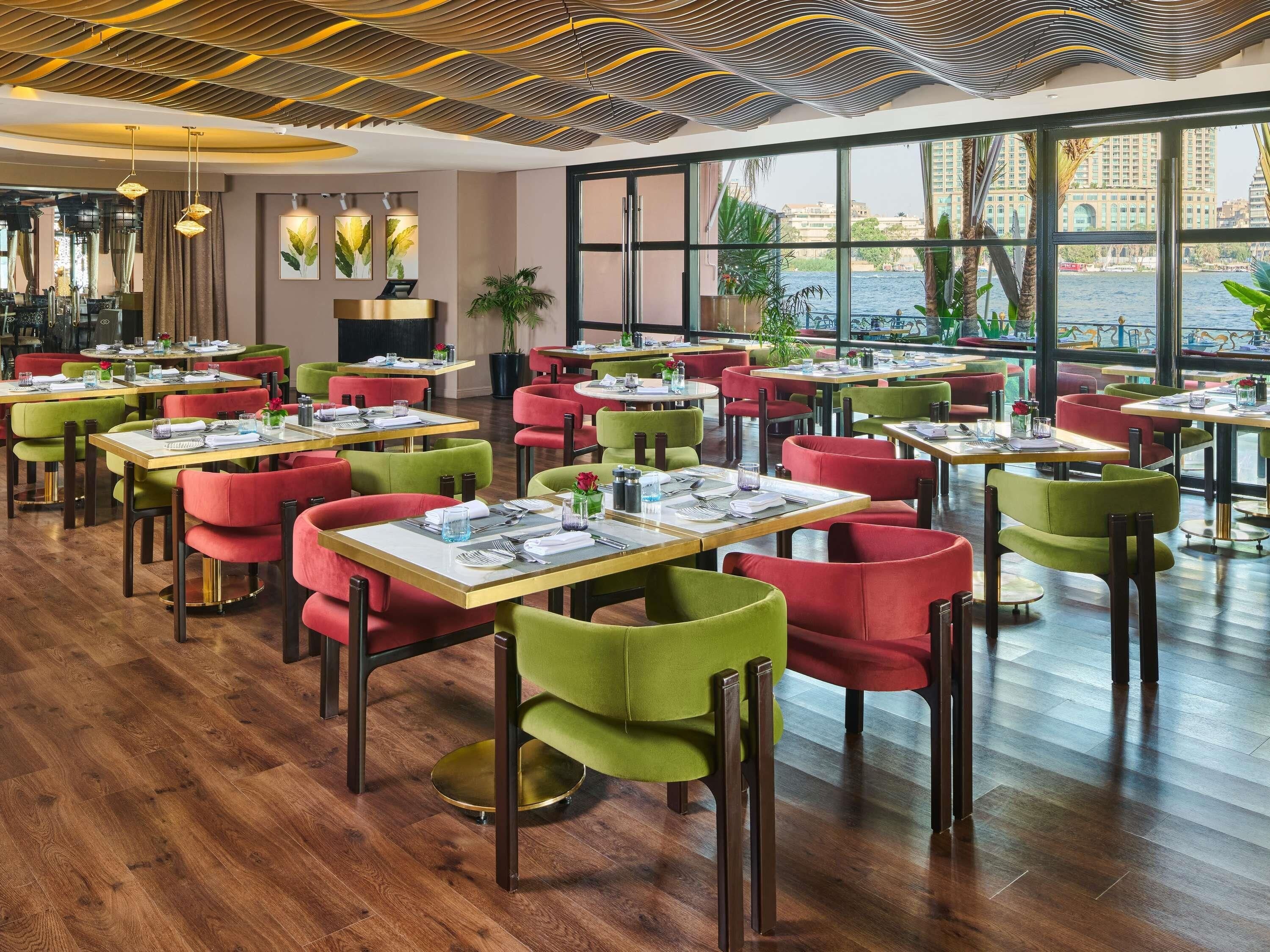 A restaurant with multiple tables and chairs, a wooden floor, and large windows offering a view of the city.