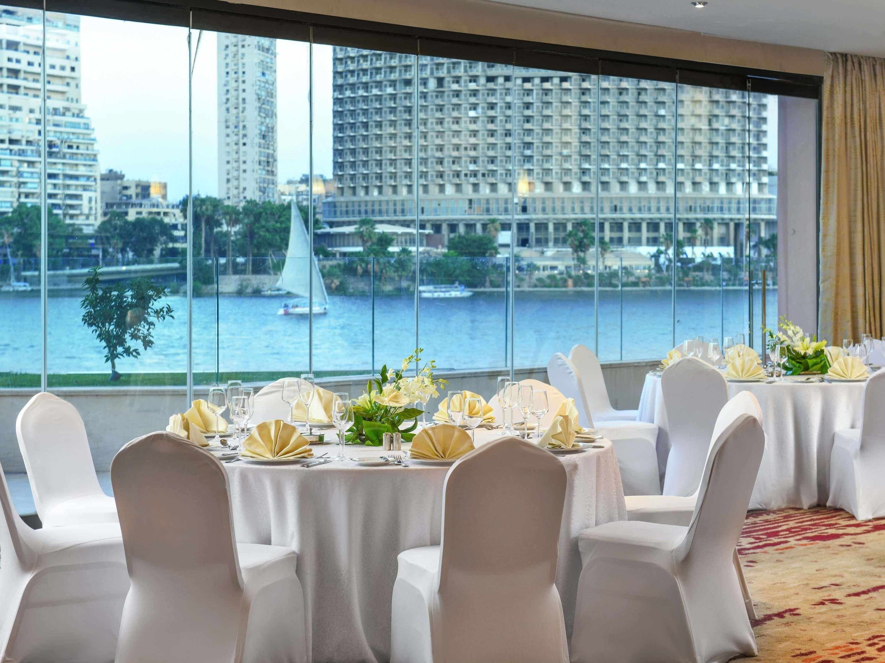 A dining area with tables set for a meal, large windows with a view of a cityscape and water.
