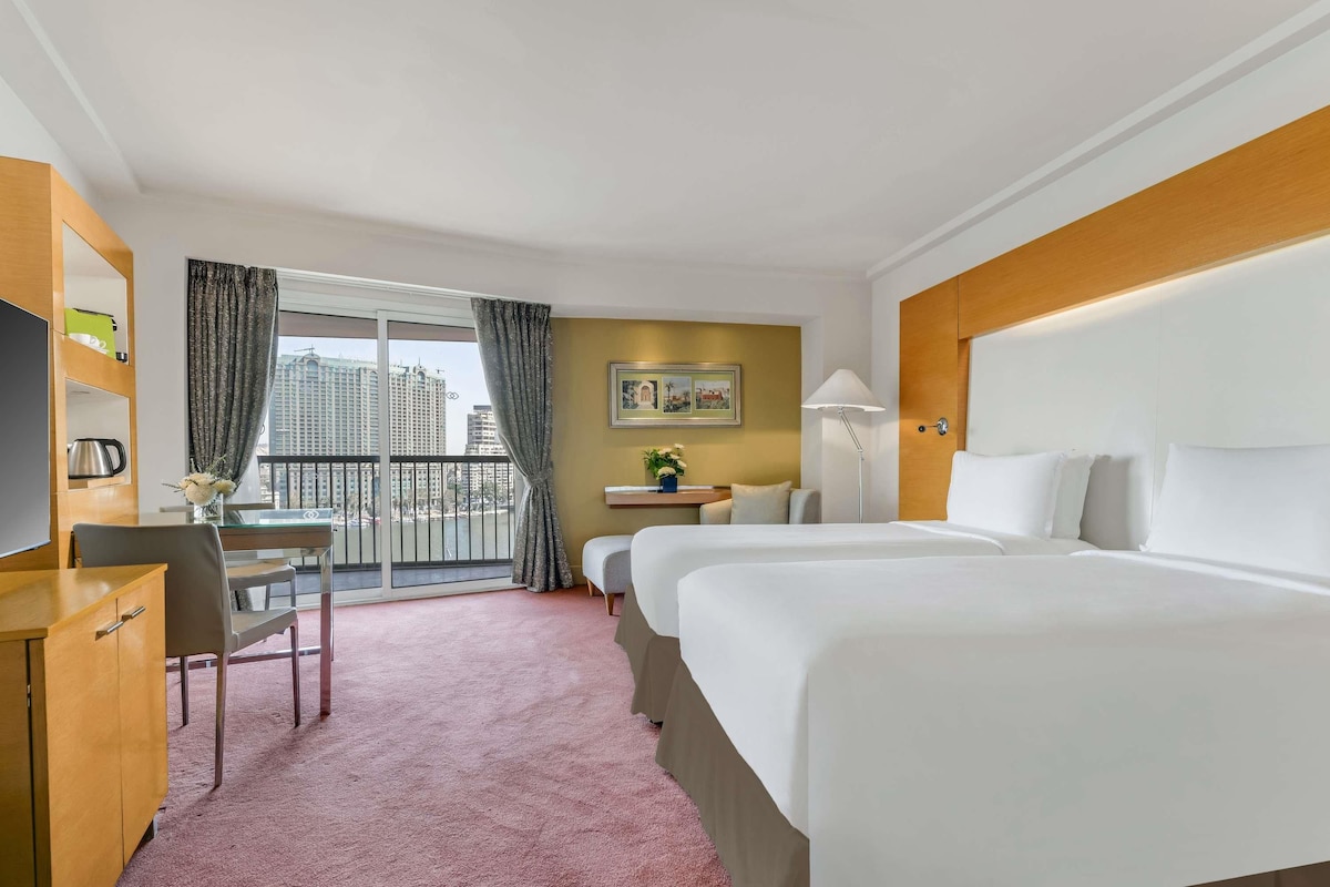 A hotel room with a bed, desk, chair, and a view of the cityscape.