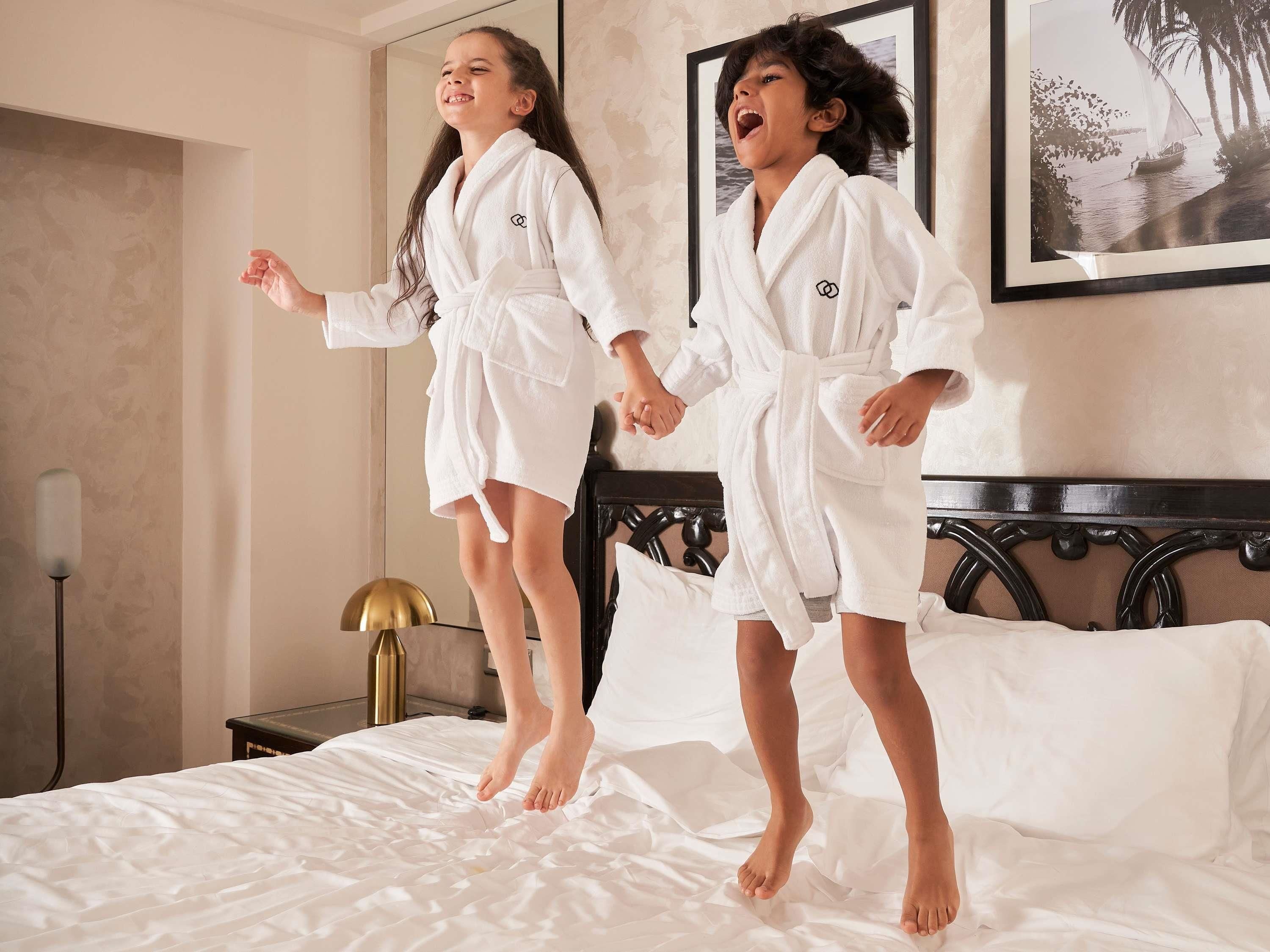 Twee personen in witte badjassen staan op een bed in een kamer met een lijst met een afbeelding aan de muur.