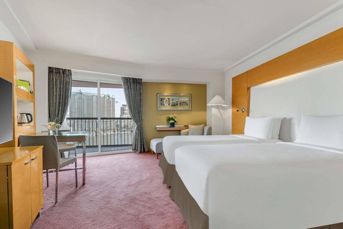 Quarto de hotel com cama, escrivaninha, cadeira e vista para a cidade.