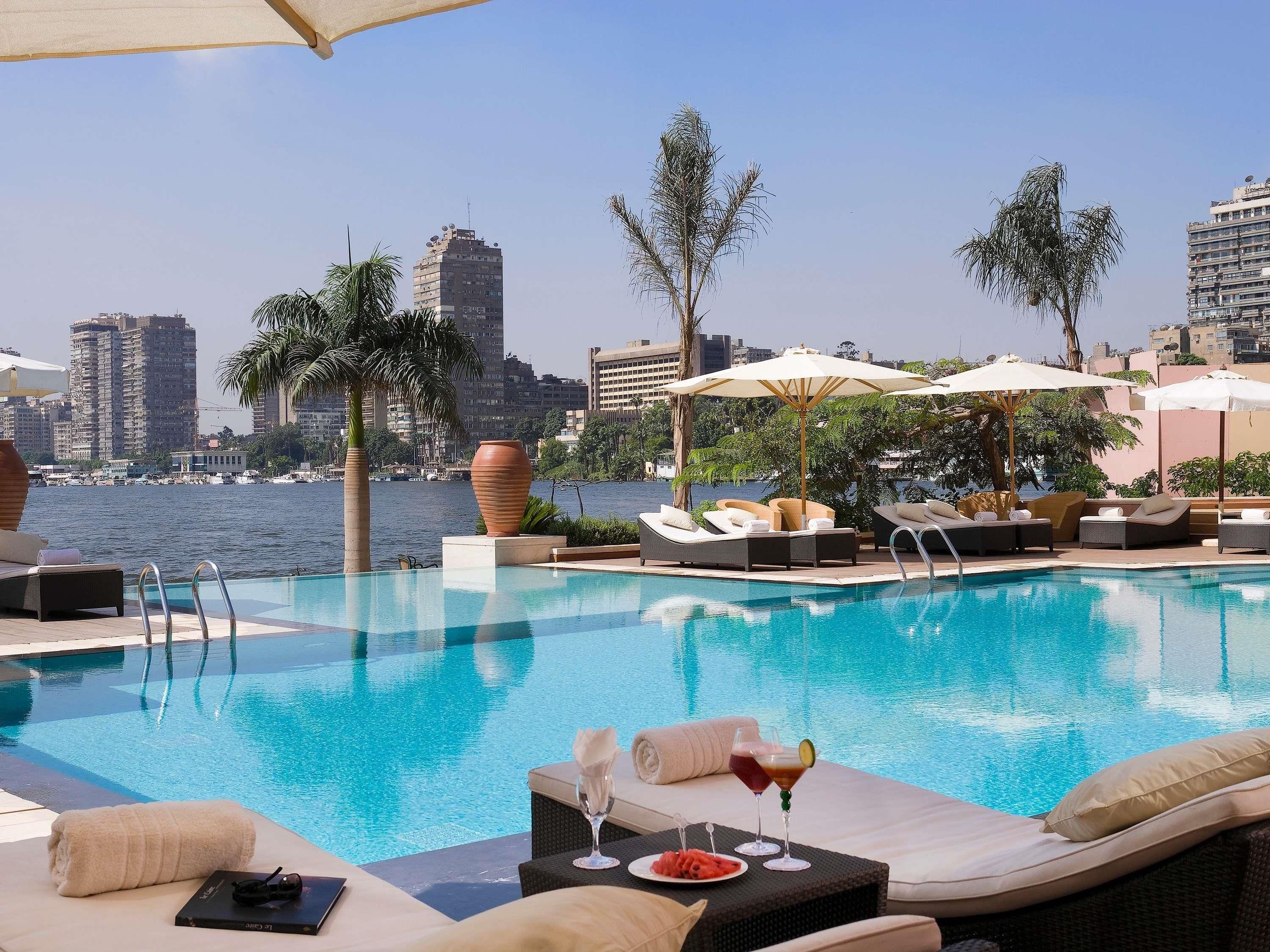 A poolside area with lounge chairs, umbrellas, and a view of the city skyline.