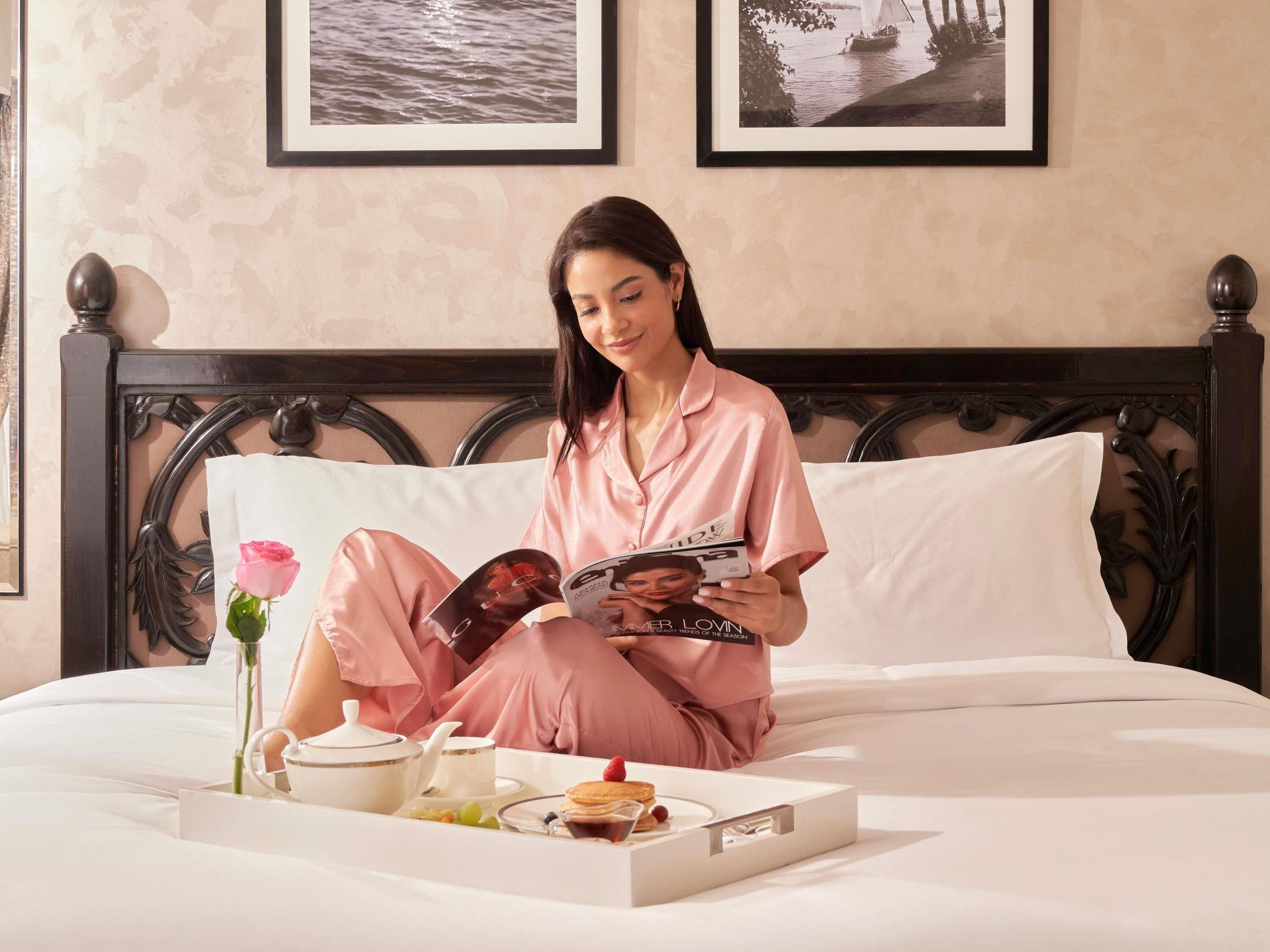 A person sitting on a bed with a tray of breakfast items, reading a magazine.